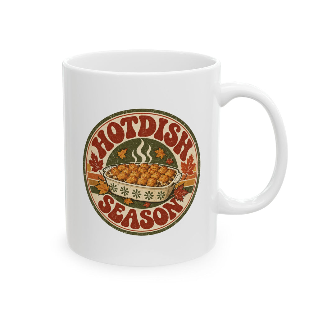A white ceramic mug with a circular retro-style graphic that reads 'HOTDISH SEASON' around an illustration of a hot casserole dish, photographed on a clean white background.