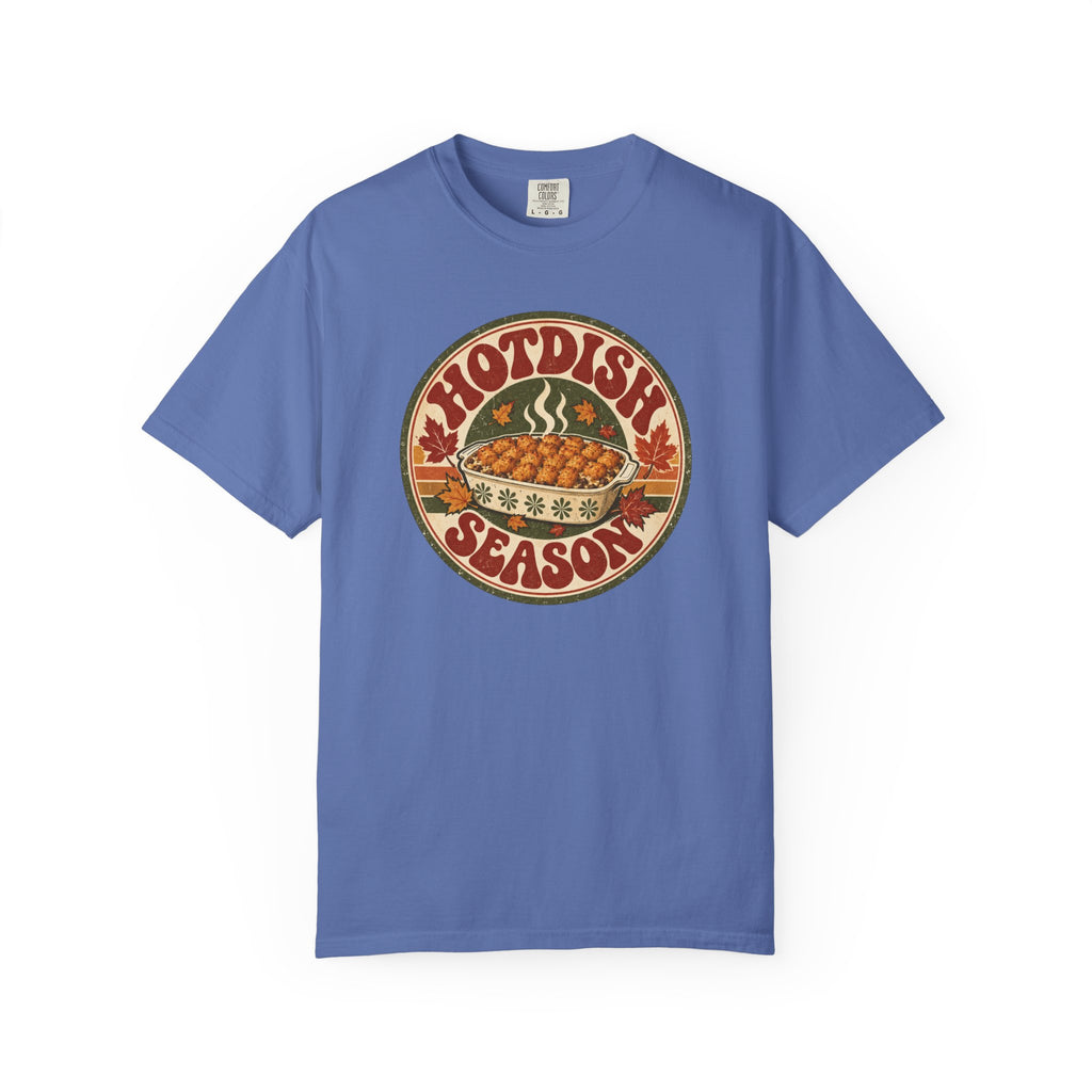 A blue t-shirt with a circular retro-style graphic that reads 'HOTDISH SEASON' around an illustration of a hot casserole dish, photographed on a clean white background.