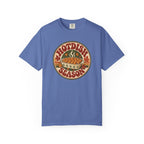 A blue t-shirt with a circular retro-style graphic that reads 'HOTDISH SEASON' around an illustration of a hot casserole dish, photographed on a clean white background.