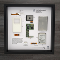 Framed display of Apple iPod 3rd generation components on a wooden surface