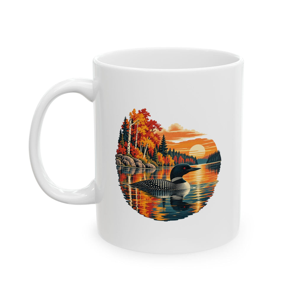 A white ceramic mug featuring a circular graphic print of a loon duck in a lake surrounded by colorful autumn trees and a sunset.