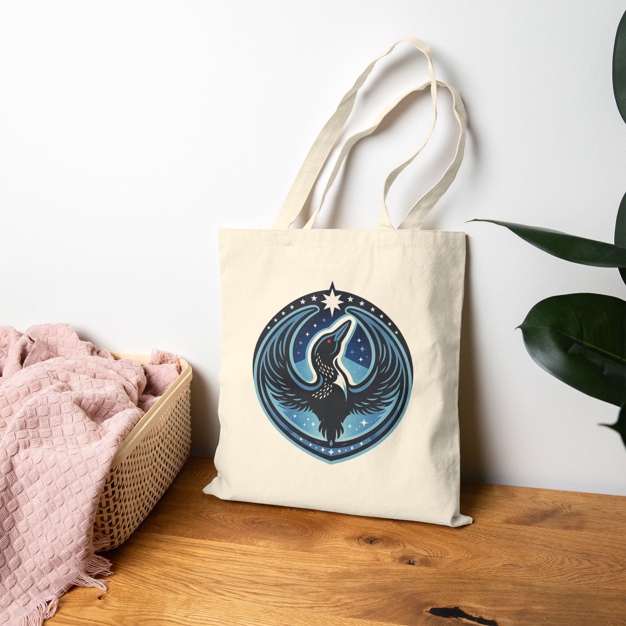 Beige tote bag with a Rebel Loon Emblem sitting next to a basket of clothes and leaning against the wall