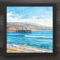 Framed artwork of a coastal scene with a pier and mountains.