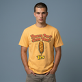A man wearing a yellow graphic t-shirt with the text 'PRONTO PUP? CORN DOG?' and 'Yes' in front of a corn dog illustration, standing against a solid gray background.
