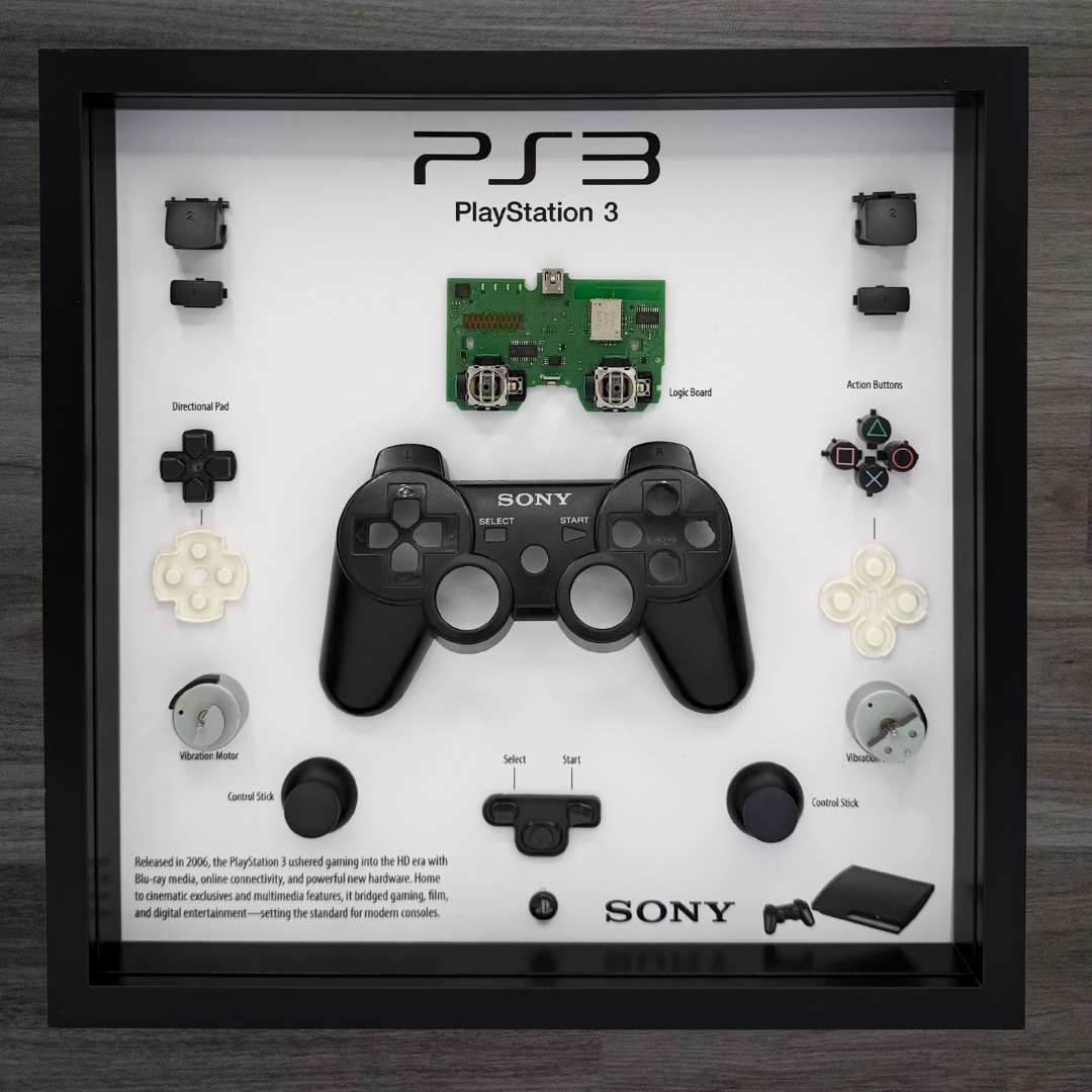 Framed display of a Sony PlayStation 3 controller and its components on a wooden surface.