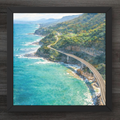 Framed artwork of a coastal road with ocean and mountains.