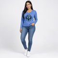 A woman modeling a blue long-sleeve V-neck t-shirt with a circular graphic on the chest, paired with blue skinny jeans and white sneakers, against a light gray studio background.