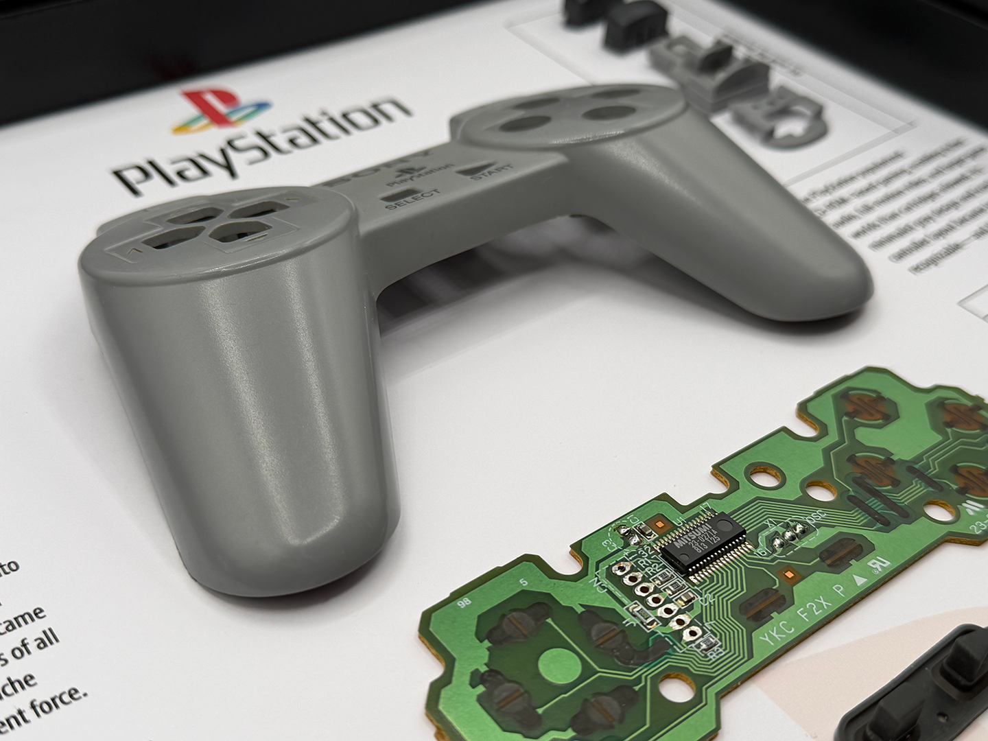 Gray gaming controller and circuit board on a PlayStation branded paper