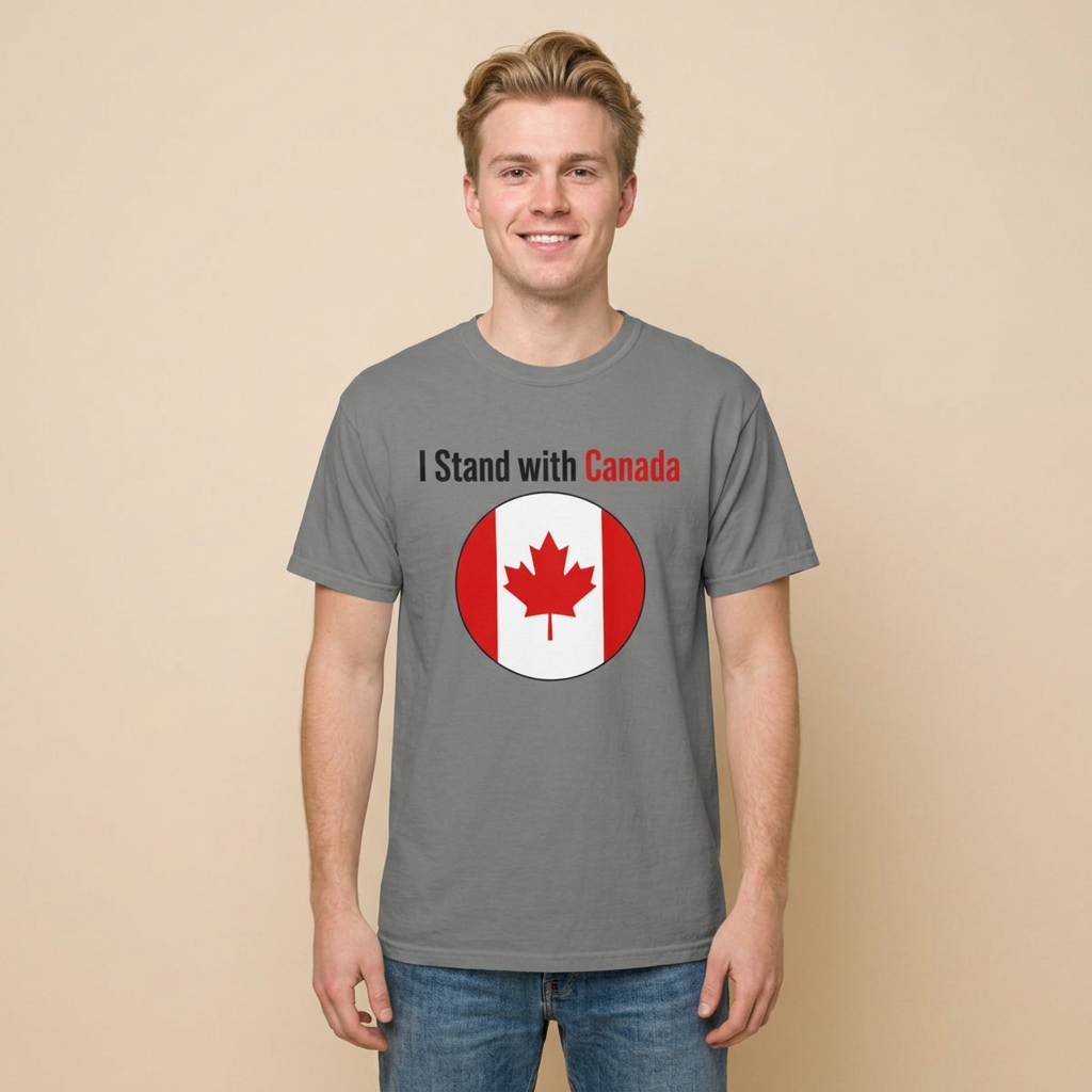 A smiling young man wearing a heather gray t-shirt with the text 'I Stand with Canada' and a circular Canadian flag graphic, paired with blue jeans, standing against a solid beige background.