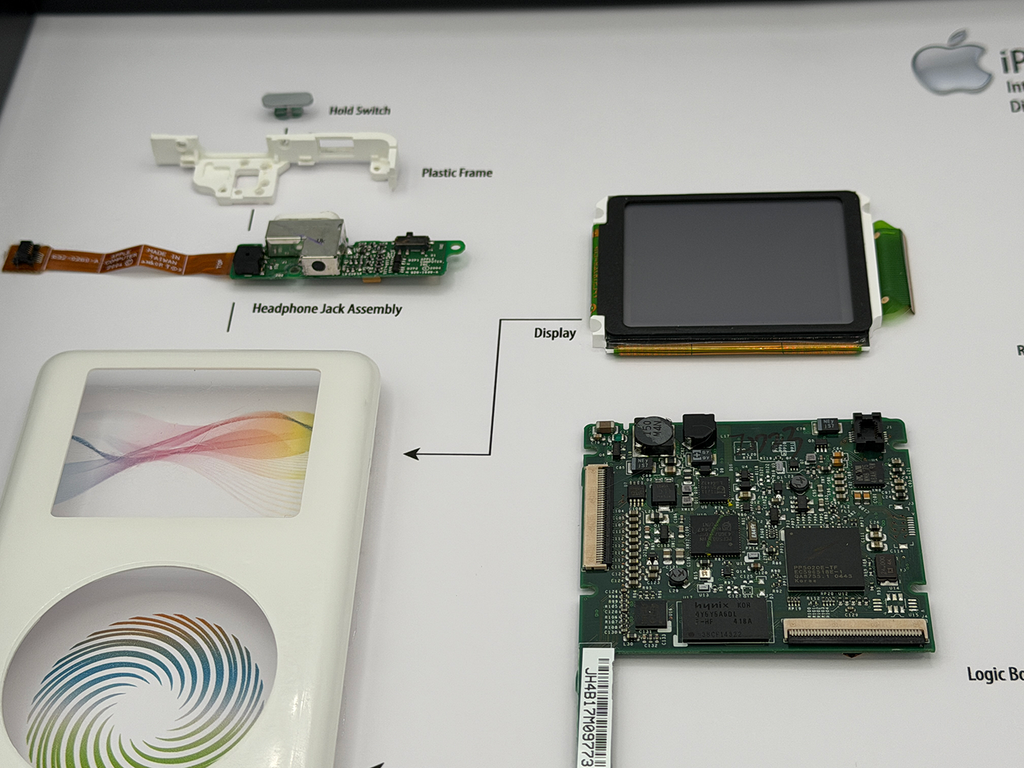 Disassembled Apple product with labeled parts on a white background
